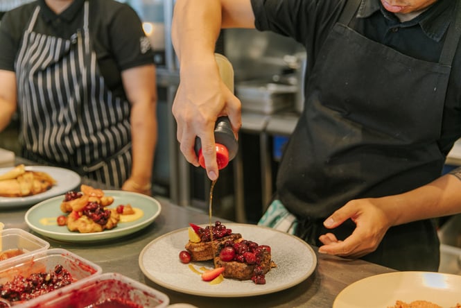 Close up of a chef drizzling syrup over a sweet meal in the kitchen at Little Pom's café, Christchurch.