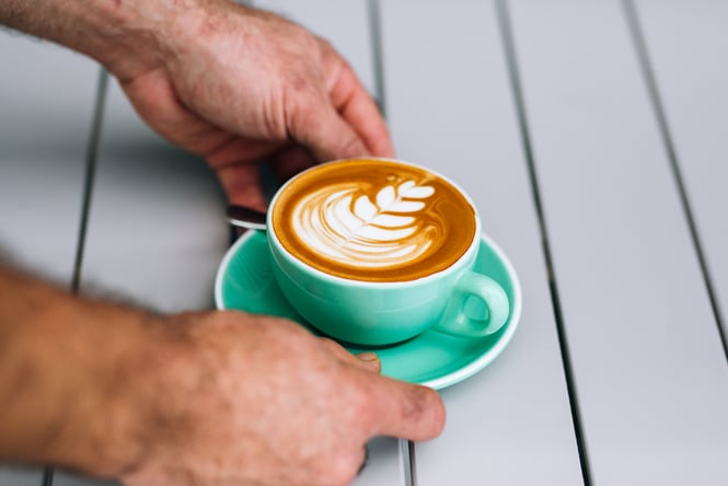 Man puts coffee on table at Manuka Brothers, Hamilton.