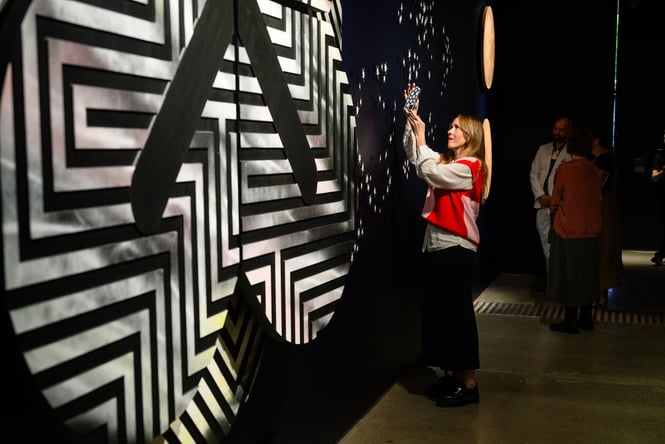 Woman looking at an exhibition and taking a photo of it at Pātaka Art + Museum.