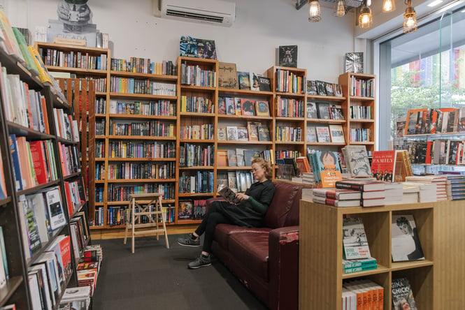 A woman sitting on a dark brown leather couch reading a book, surrounded by bookshelves, in Scorpio Books.