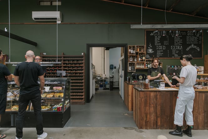 Customers standing around at a counter inside a green decorated cafe.