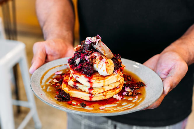 Man holding a plate of hotcakes with berries from t bay cafe, Porirua.