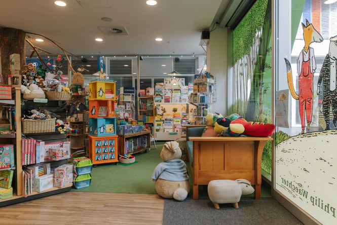 Books and toys on shelves and a couch with big soft toys at Telling Tales children's bookshop, Christchurch.