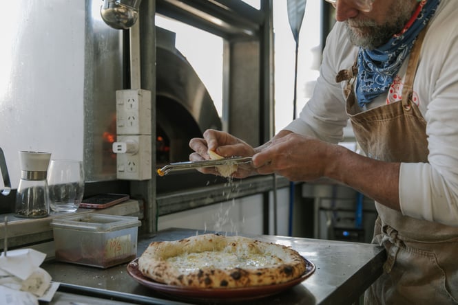 Cheese being grated onto a pizza at Bomba.