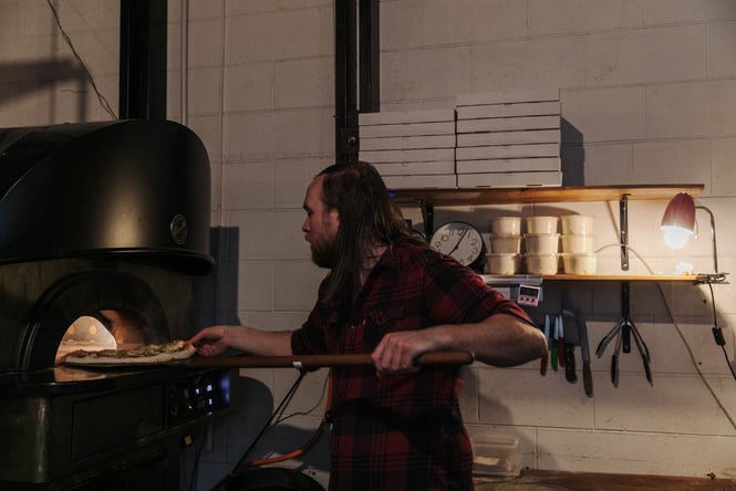 Pizza maker putting the pizza in the woodfired oven at Pizza Trap.