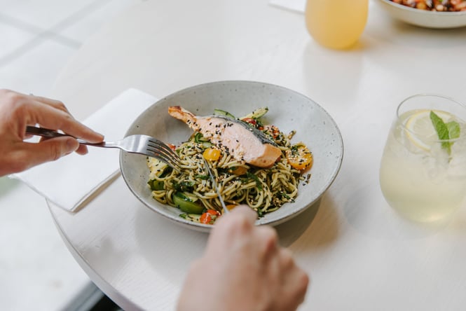 Someone digging into a plate of salmon and noodles with a knife and fork