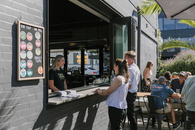 Two people ordering at an open bar window.