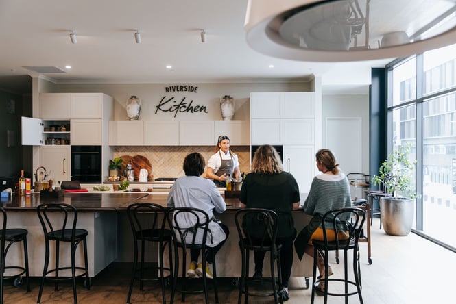Group of people watch a cooking demonstration at Riverside Kitchen.