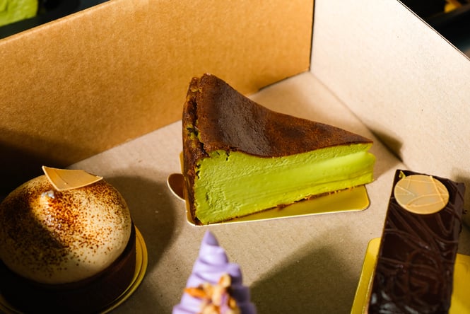 Matcha basque cheesecake inside box next to other pastries and desserts