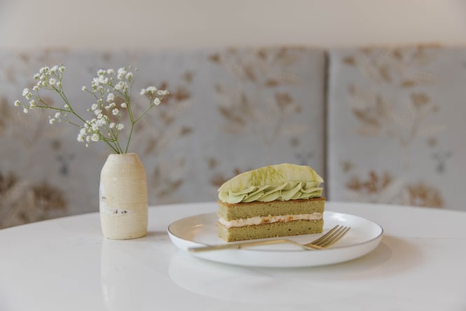 Beautiful matcha patisserie with layers of matcha sponge, mandarin jam, and a tempered white chocolate garnish