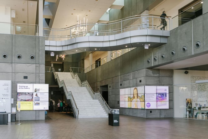 In the foyer of the Christchurch Art Gallery where someone is crossing the floating bridge on the second floor.
