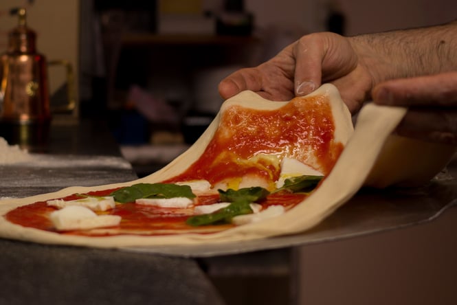 Pizza dough being shaped with tomato sauce and basil on top.