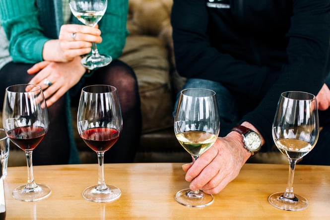 A close up of two people sitting behind glasses of white and red wine.