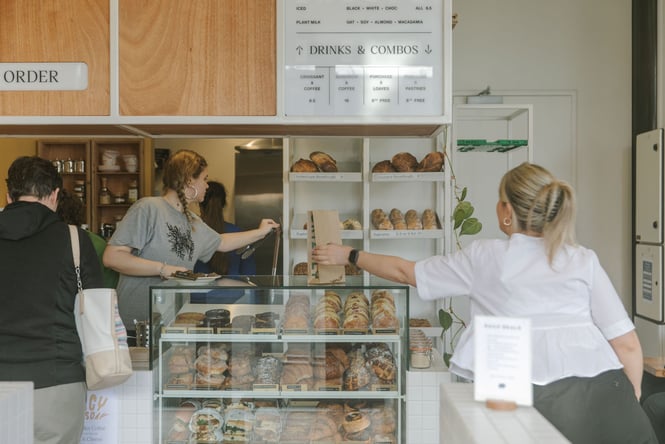Grizzly worker serving customers next to cabinet of pastries and sandwiches and a shelf of sourdough bread