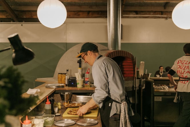 Chef making pizza next to wood-fired oven at Lillies in Christchurch