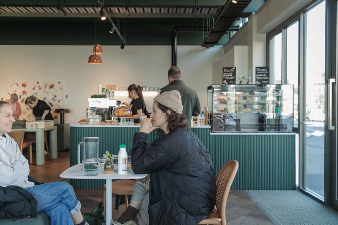 Two women sitting together at Swoon cafe with shop and green cafe counter in the background