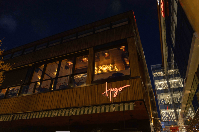 Exterior of Hugo restaurant building along the Terrace with sign lit up at night