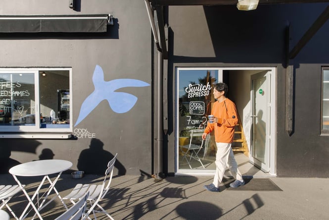 Barista walking out door of Odds Coffee with takeaway coffee in hand