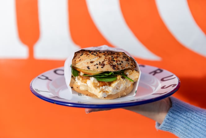 Close up of Eggy Breakfast bagel at Grizzly against a bright orange wall
