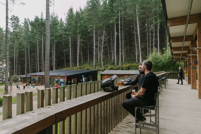 Two men sitting at the bench having a beer looking out over the park.