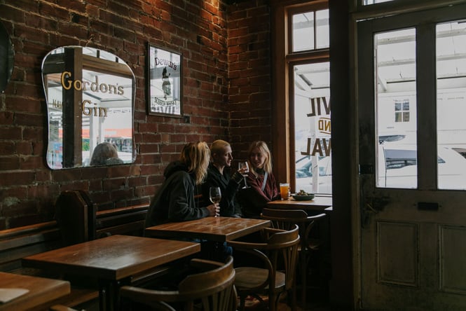 Three people sitting by the window at Civil Naval having a glass of wine.