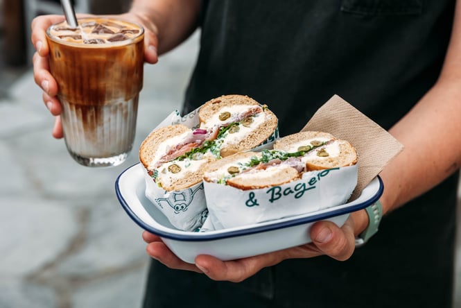 Customer holding a bagel in one hand and an iced coffee in the other hand at Curbside.