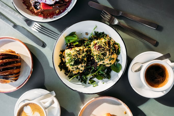 Birds eye view of an eggs dish at Scroggin on a table with white and black coffees, a croissant and plate of waffles.