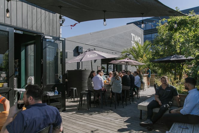 Customers sitting at outdoor tables under umbrellas in the sun.