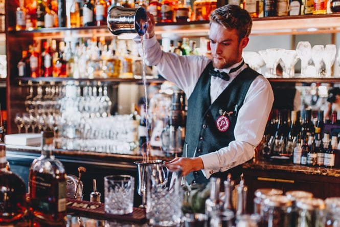 Bartender at speakeasy pouring flaming liquid into cocktail