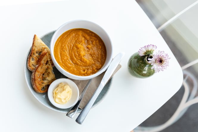 Carrot and ginger soup on cafe table with bread next to flowers in small vase