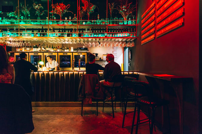 A man and woman sitting on high stools at a darkly lit bar.