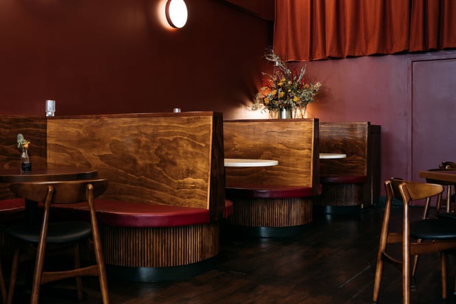 Wooden booths with maroon upholstery against maroon-coloured walls and curtains inside The Ram.