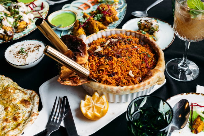 Large biryani dish in the foreground with other dishes in the background.