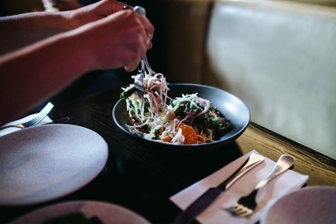 Hands dishing out a salad from a bowl.