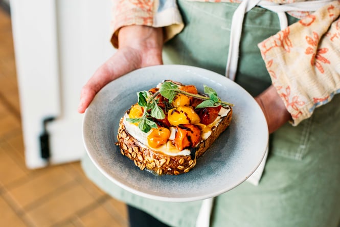 Hands holding a plate of tomato on toast.