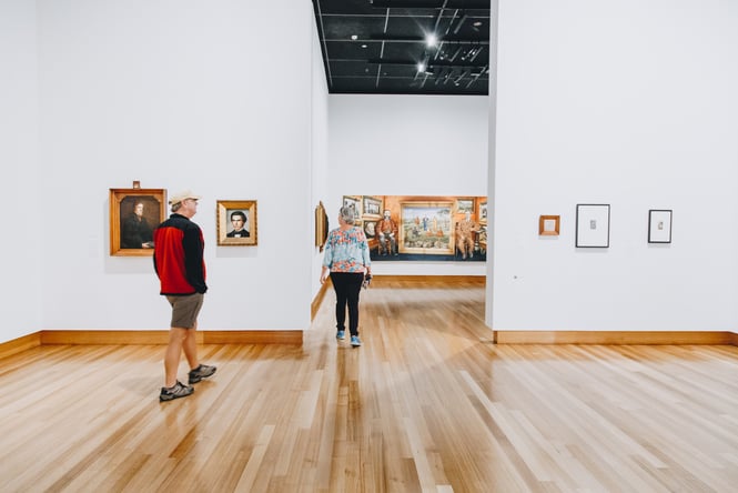 A man and a woman strolling around a light and bright exhibition room inside Christchurch Art Gallery.