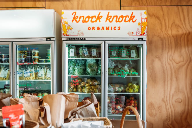 Fridge in a shop containing fresh vegetables and other items.