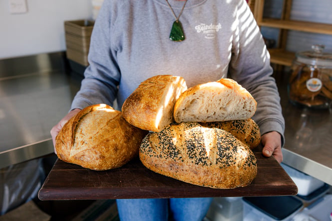 Baker holding a tray of freshly baked sourdough loaves.