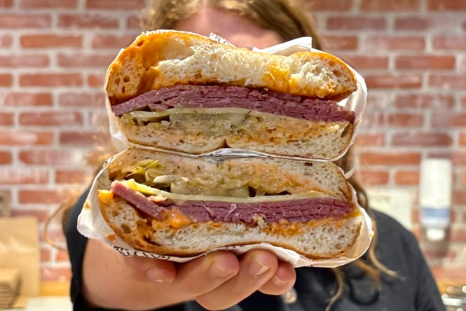 Filled bagel cut in half being held by a staff member at Downtown Bagels