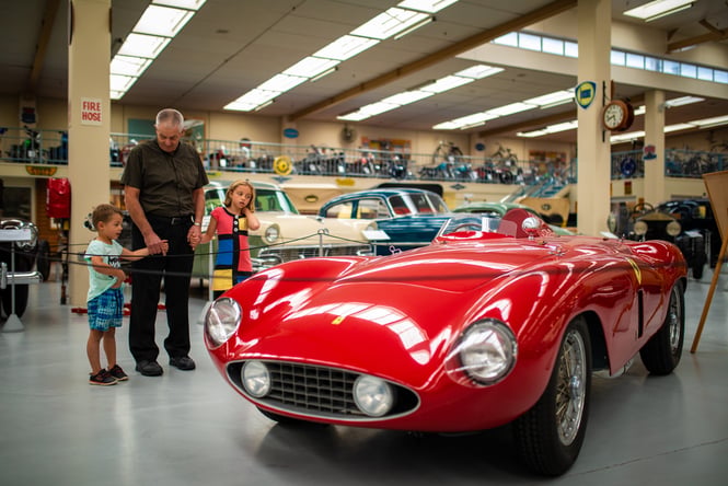 Children with their grandfather looking at a red car.
