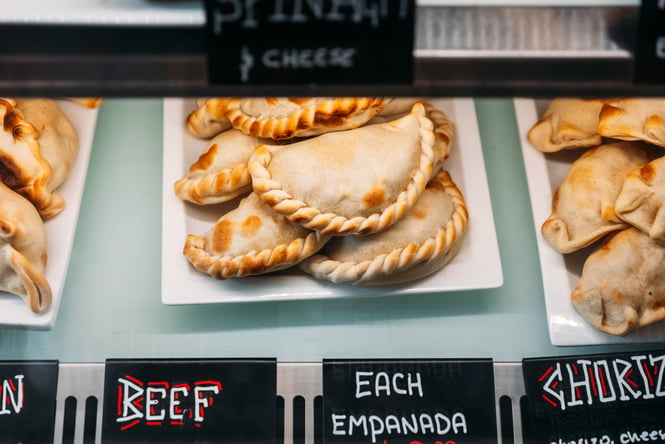 A close up of empanadas in a glass counter.