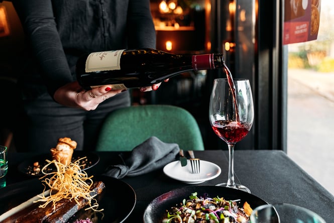Glass of wine being poured with other dishes on the table.