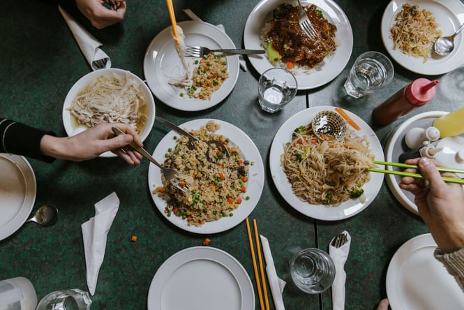 Table full of Chinese noodles and rice with diners tucking in with chopsticks