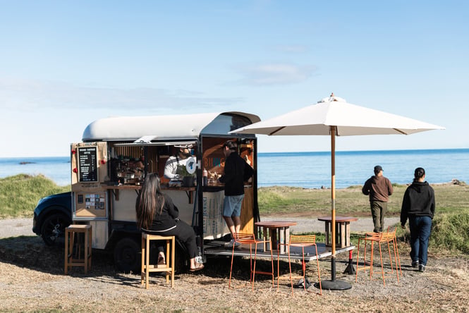 Customers waiting to order in front of a coffee cart with the beach in the background.