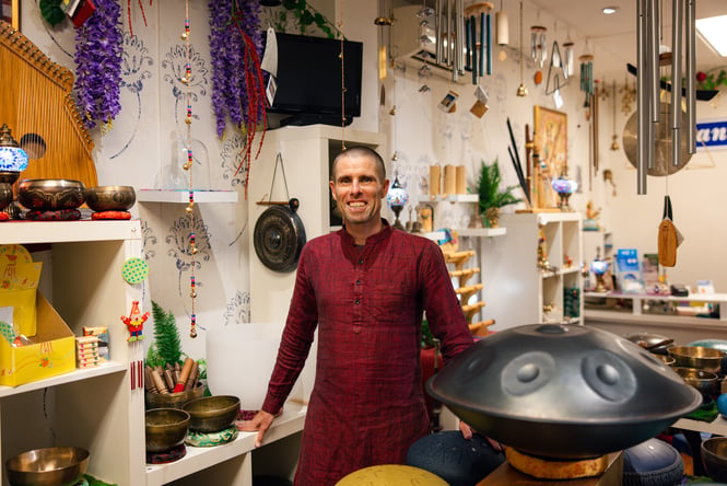A man wearing red inside a music store smiling to camera.