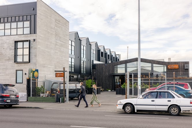 People walking on a footpath in front of a grey building.