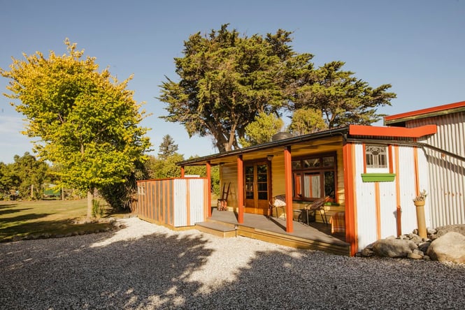 A tiny orange cottage sitting next to a gravel road on a sunny day.