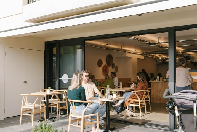 Two people sitting outside in the sun enjoying coffee at a cafe