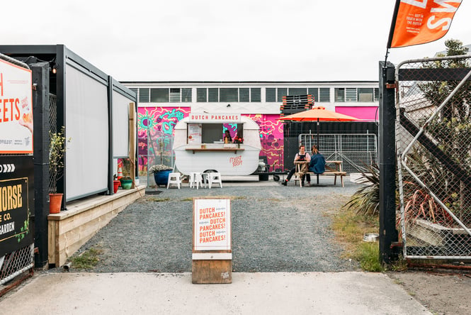 A food caravan and container cafe around a gravel lot with outdoor seating.