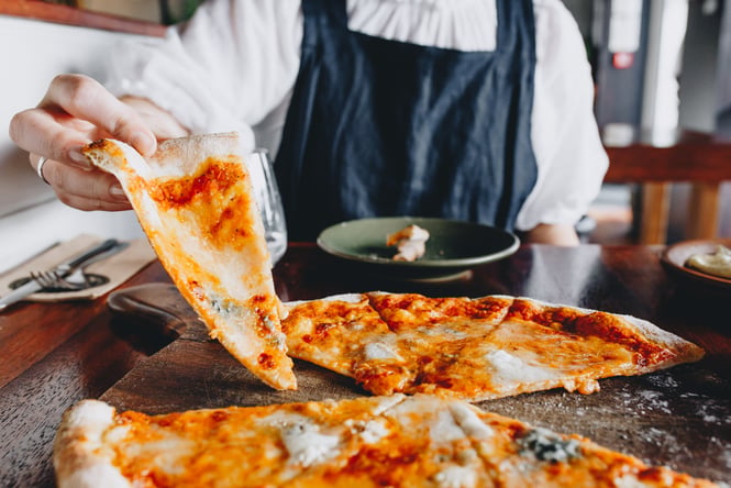 A woman's hand holding a slice of tomato and cheese pizza.